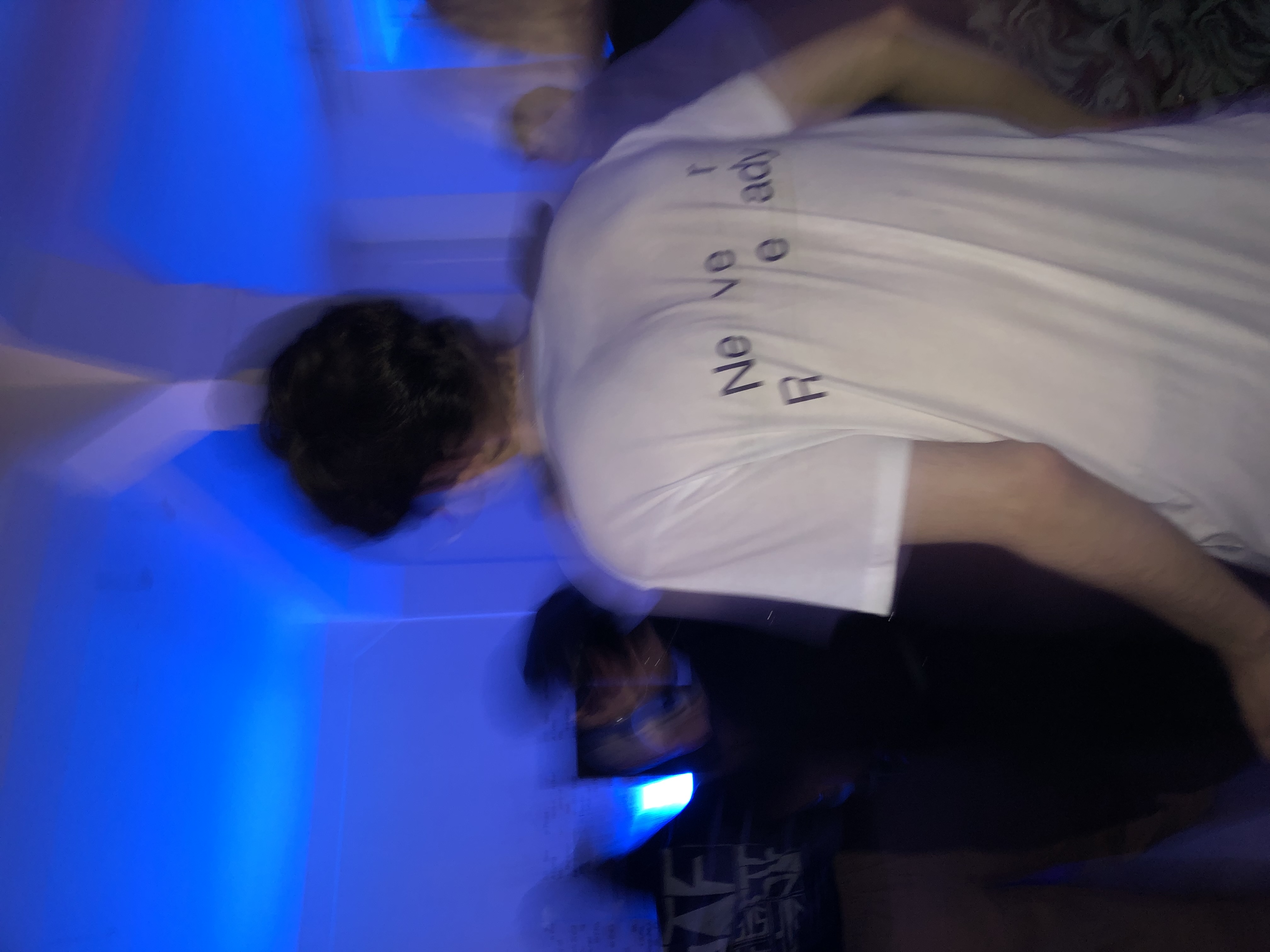 The back of a white t-shirt with black letters was captured in motion, immersed in blue light.